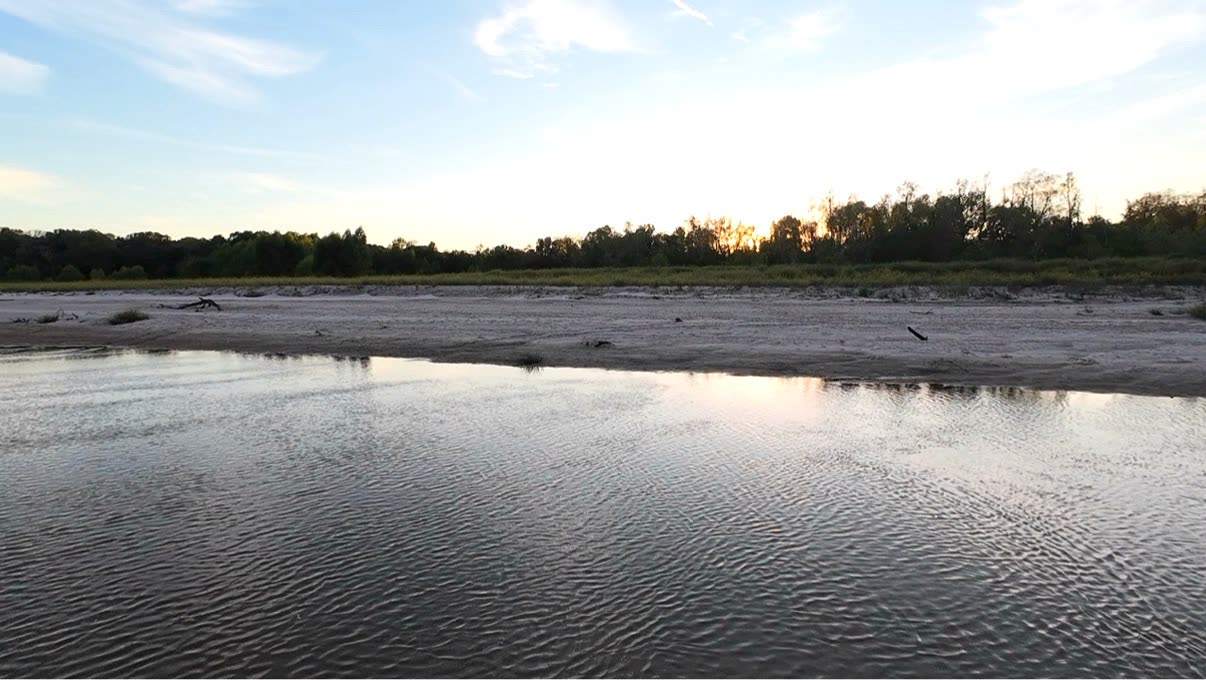 Riverside sunset with a gradient sky reflected on the water beside a white-sand beach
